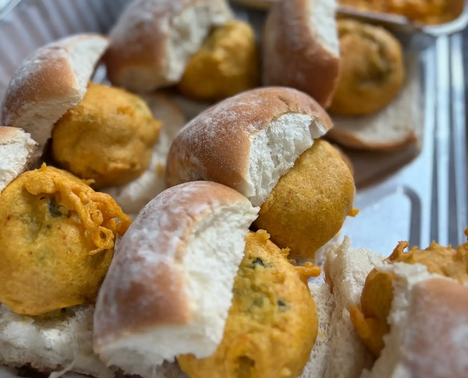 Vada pav in a foil catering tray: each pav split open around a golden potato fritter.